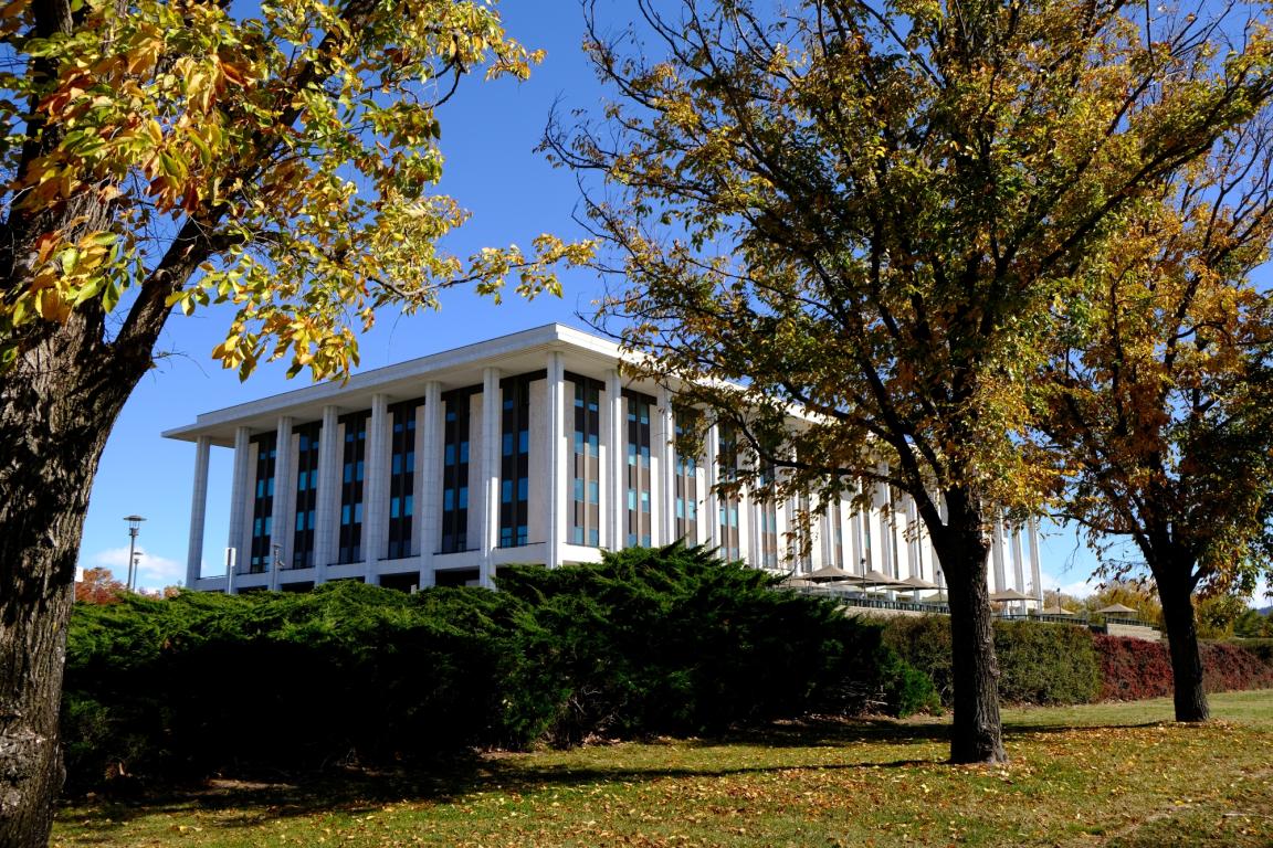 The National Library of Australia building is in the centre of this image. Trees with yellowing autumnal foliage are in the foreground.