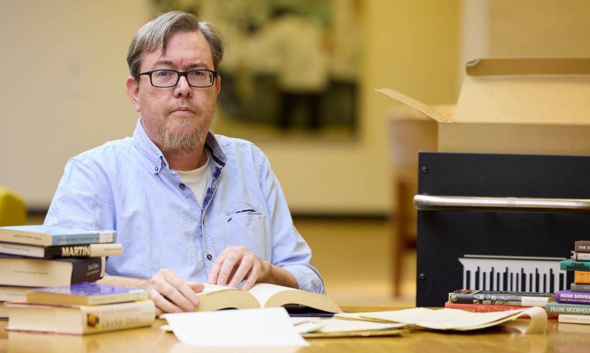 A man  with glasses wearing a black button-down shirt in the National Library of Australia's Special Collections Reading Room