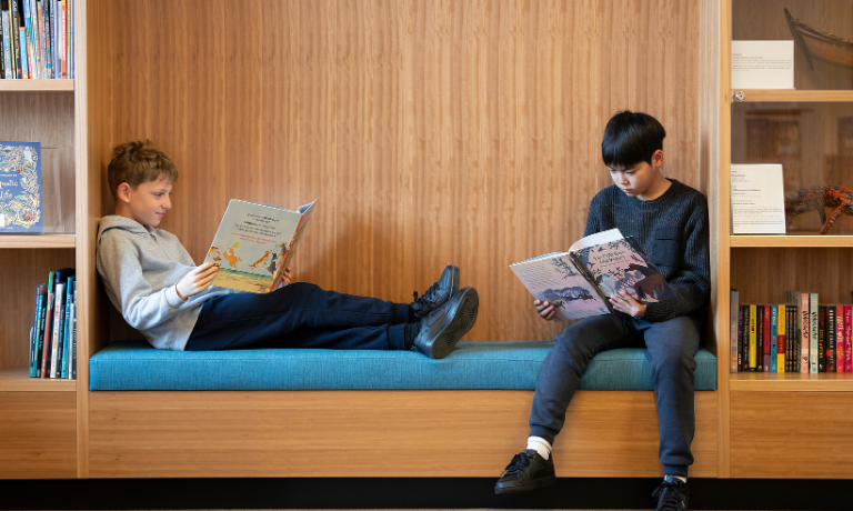 Two boys, sitting on a couch that is built into a book shelf