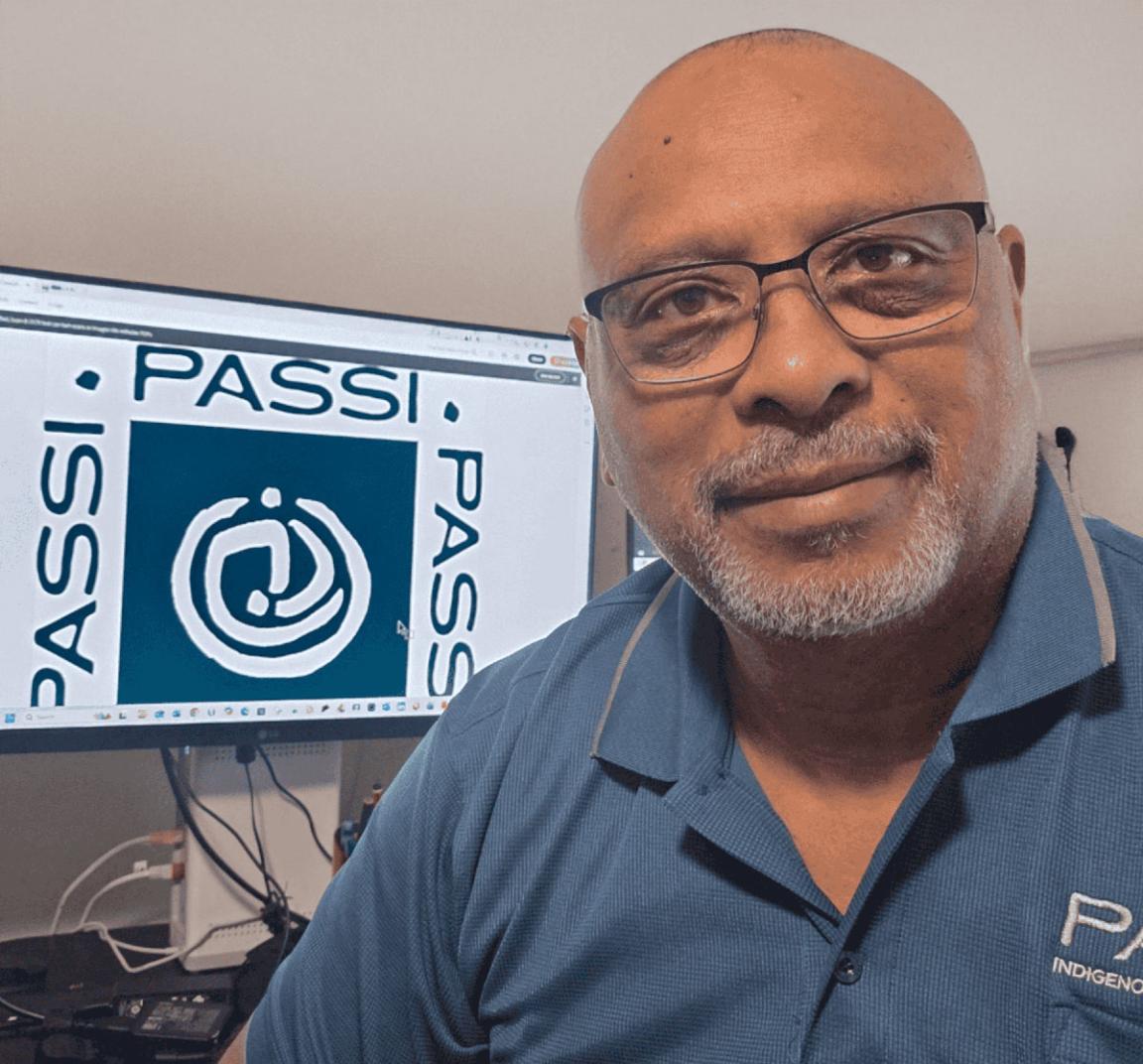 Michael Passi in a blue polo shirt, with a computer screen behind him to his left with the Passi Logo