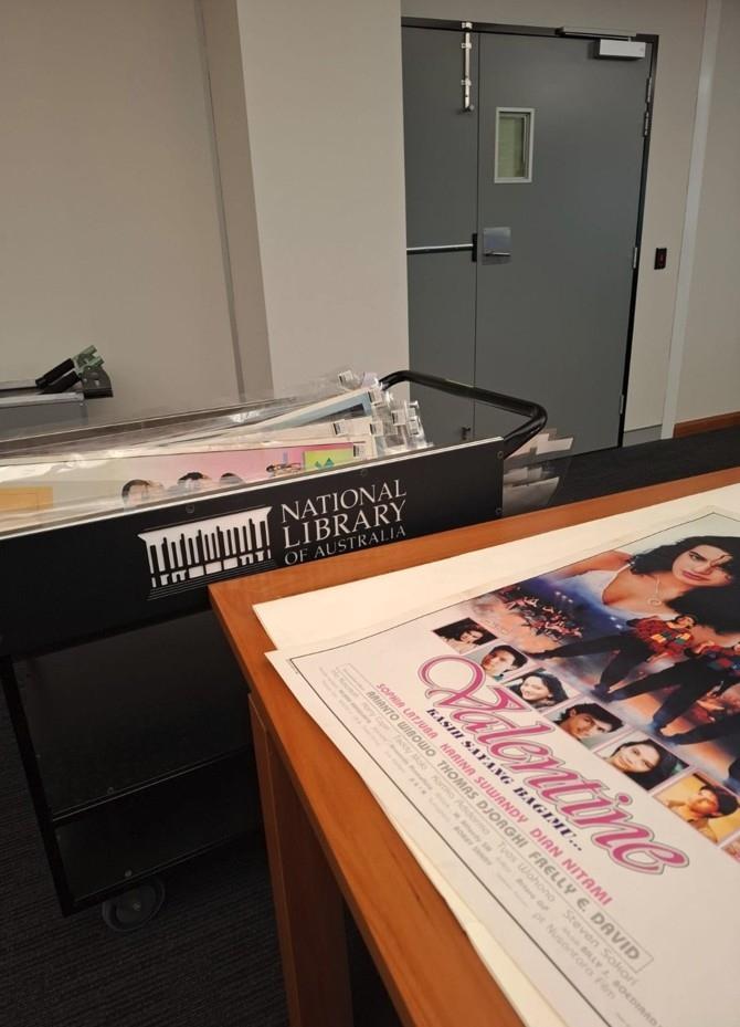 A National Library of Australia branded black trolley and a stack of Indonesian film posters in the Special Collections Reading Room