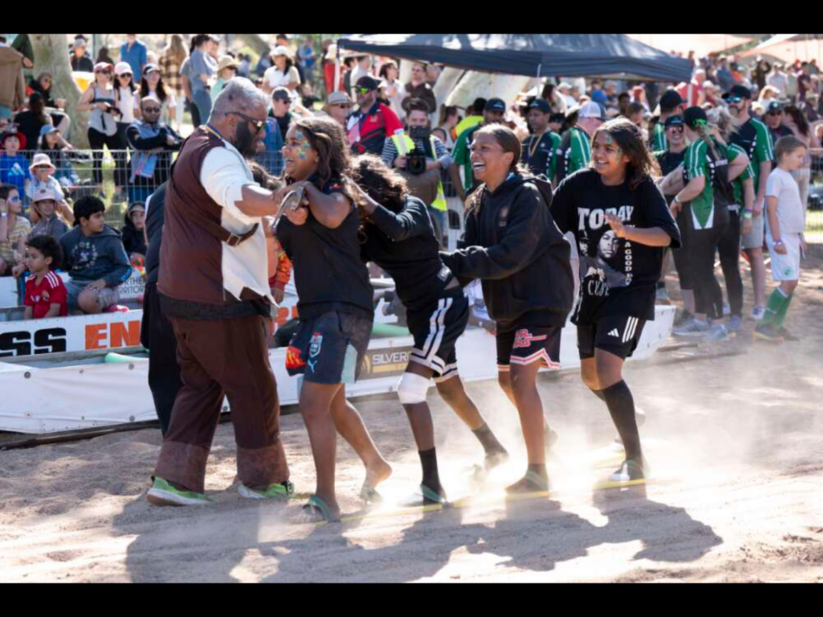 A group of young people laugh as they participate in an outdoor race on a dusty riverbed. 