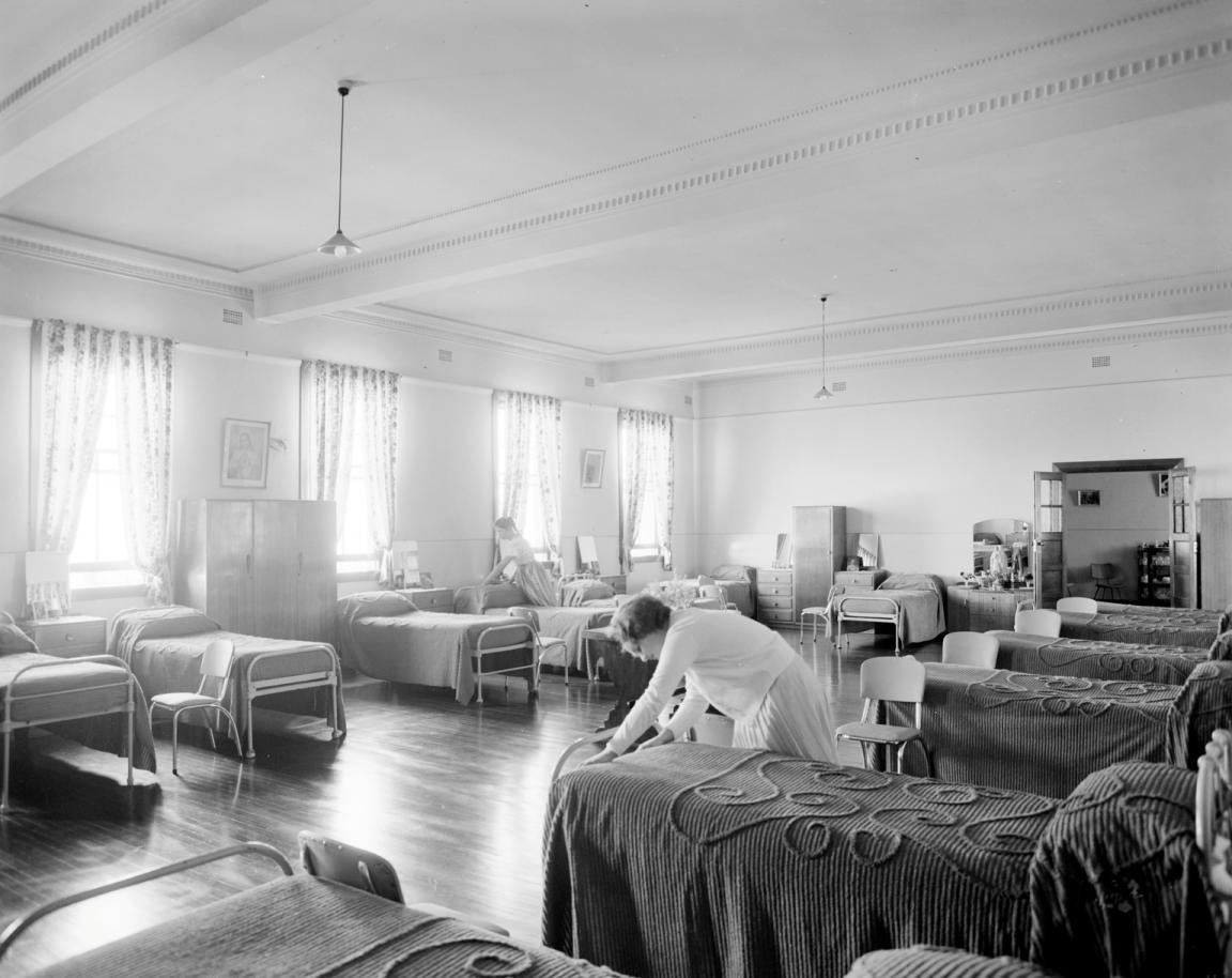 Black and white photo of a girl making a bed in a dormitory