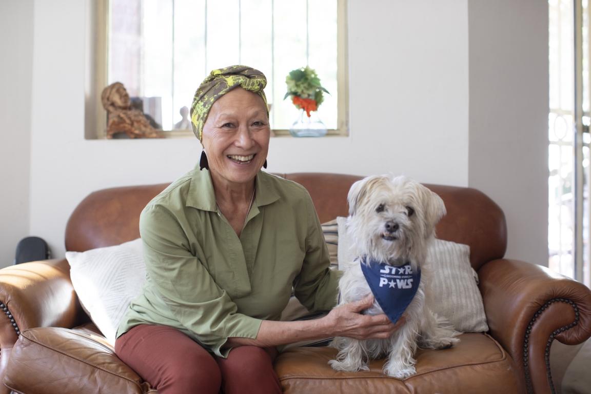 Chinese-Australian woman Saulan Beverly Yin-Lo smiling and sitting on a brown leather couch with a small white dog
