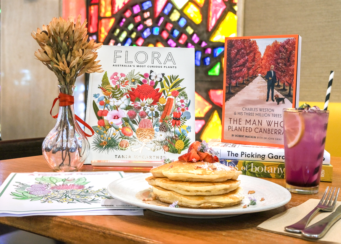 Table at Bookplate cafe with special menu items, kids activity sheets and books for Floriade with colourful stained glass windows in the background