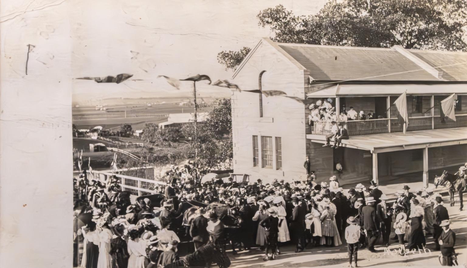 Front of an old postcard with a black and white photo of crowds gathered around a building