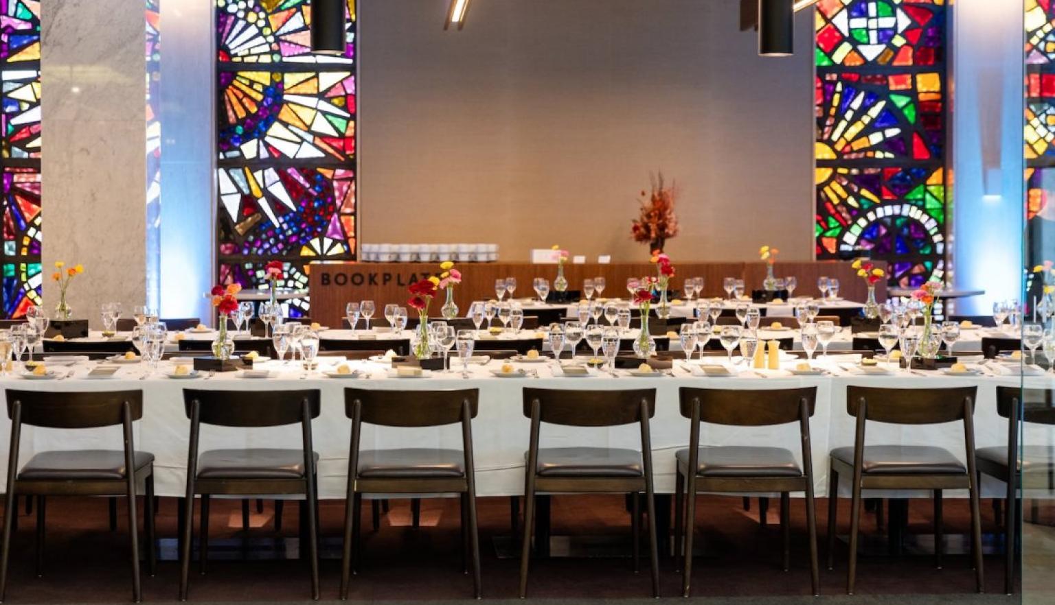 Bookplate cafe at the Library set up with long tables set with white table cloths, wine glasses and flowers