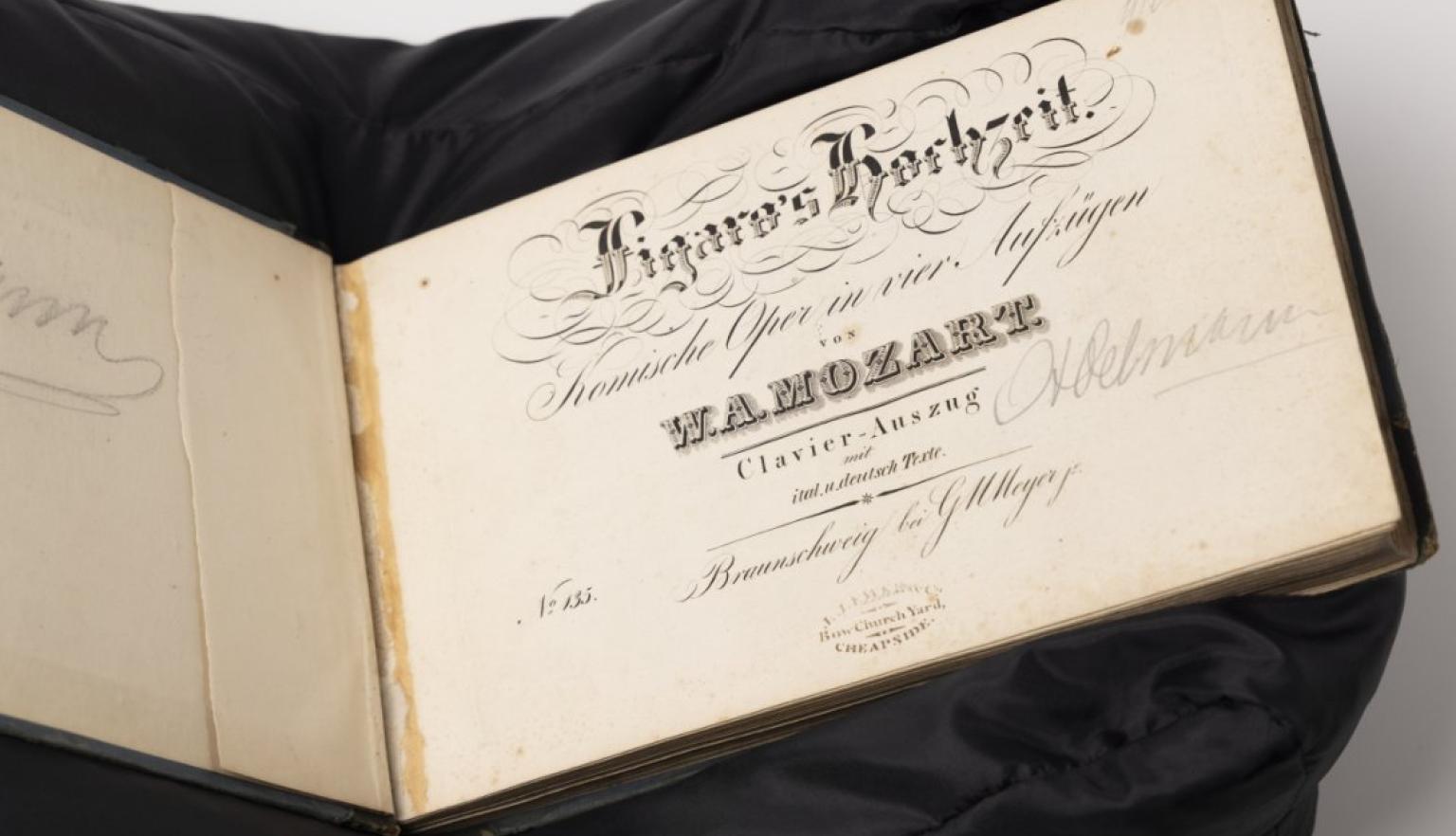 An open oblong music score open to the title page, sitting on a black cushion