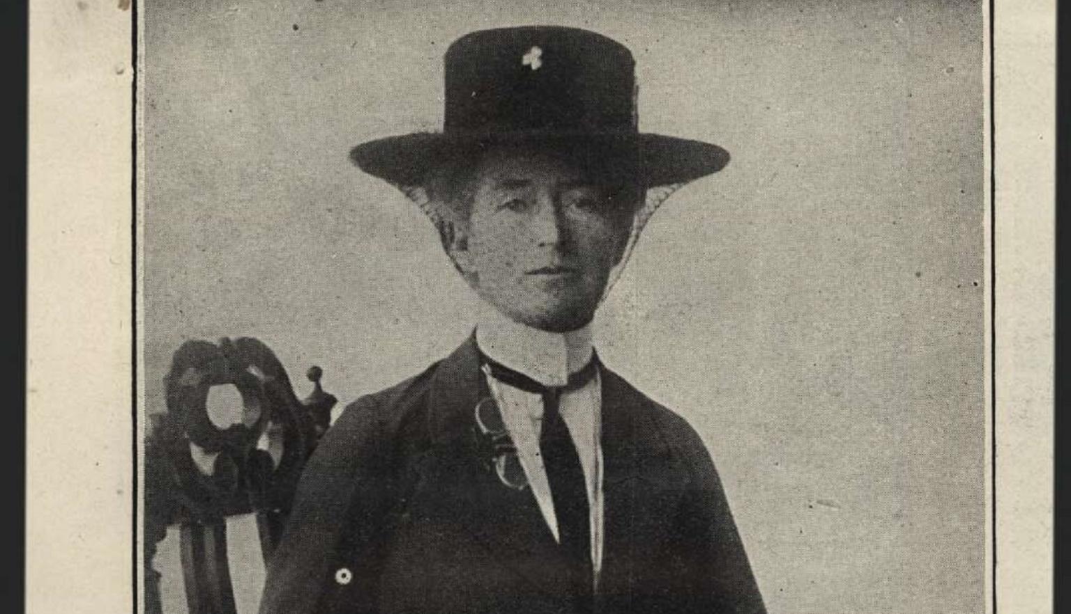 Black and white headshot of Mrs Daisy M. Bates, wearing a black hat and tie while sitting on a chair. 