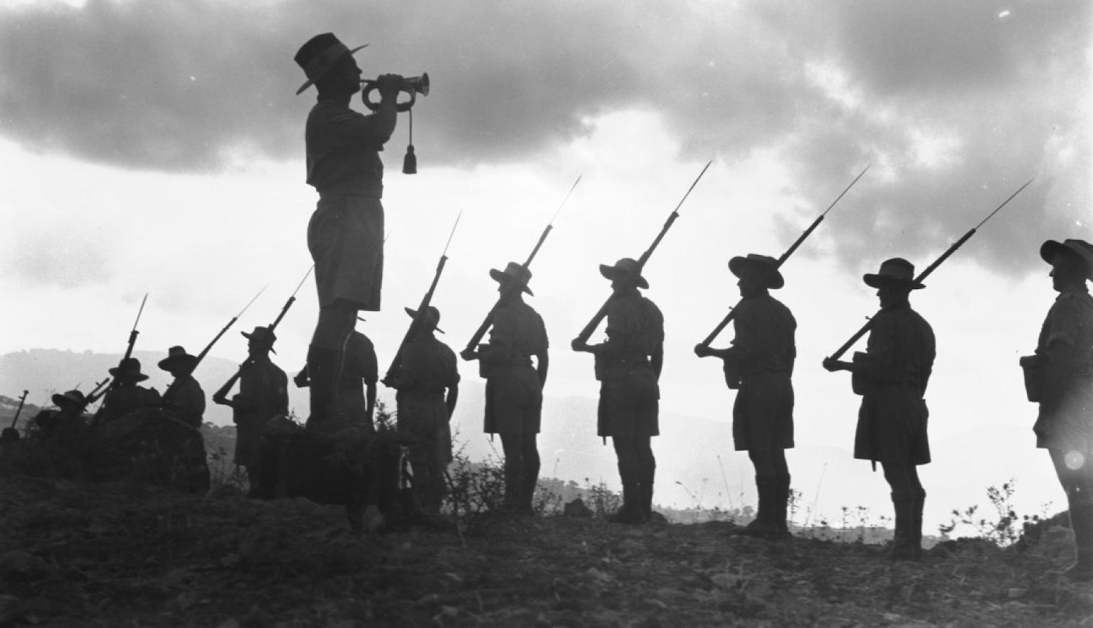 Man with a trumpet standing near a row of soldiers holding rifles over their shoulders