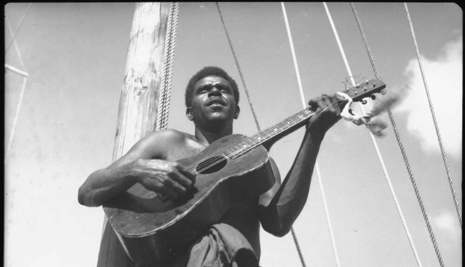A black and white photo of a man playing a guitar on a boat