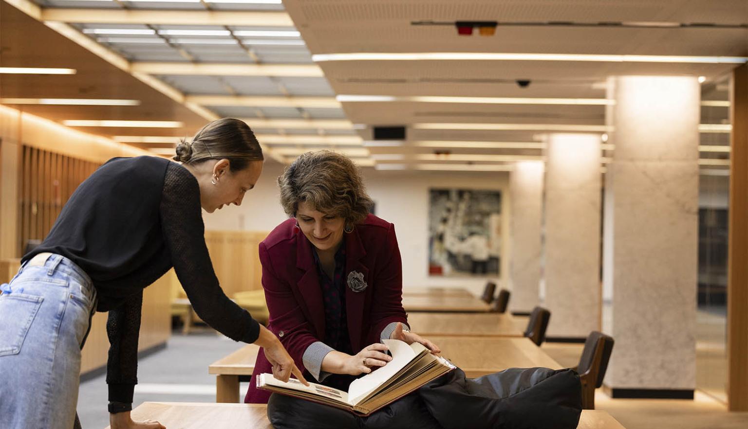 Two people bending over a desk and looking at a book.