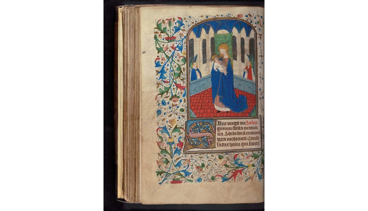 A handwritten page from a book of hours. The page is highly decorated and brightly coloured. An image of a woman holding a baby is framed by leaves and vines.