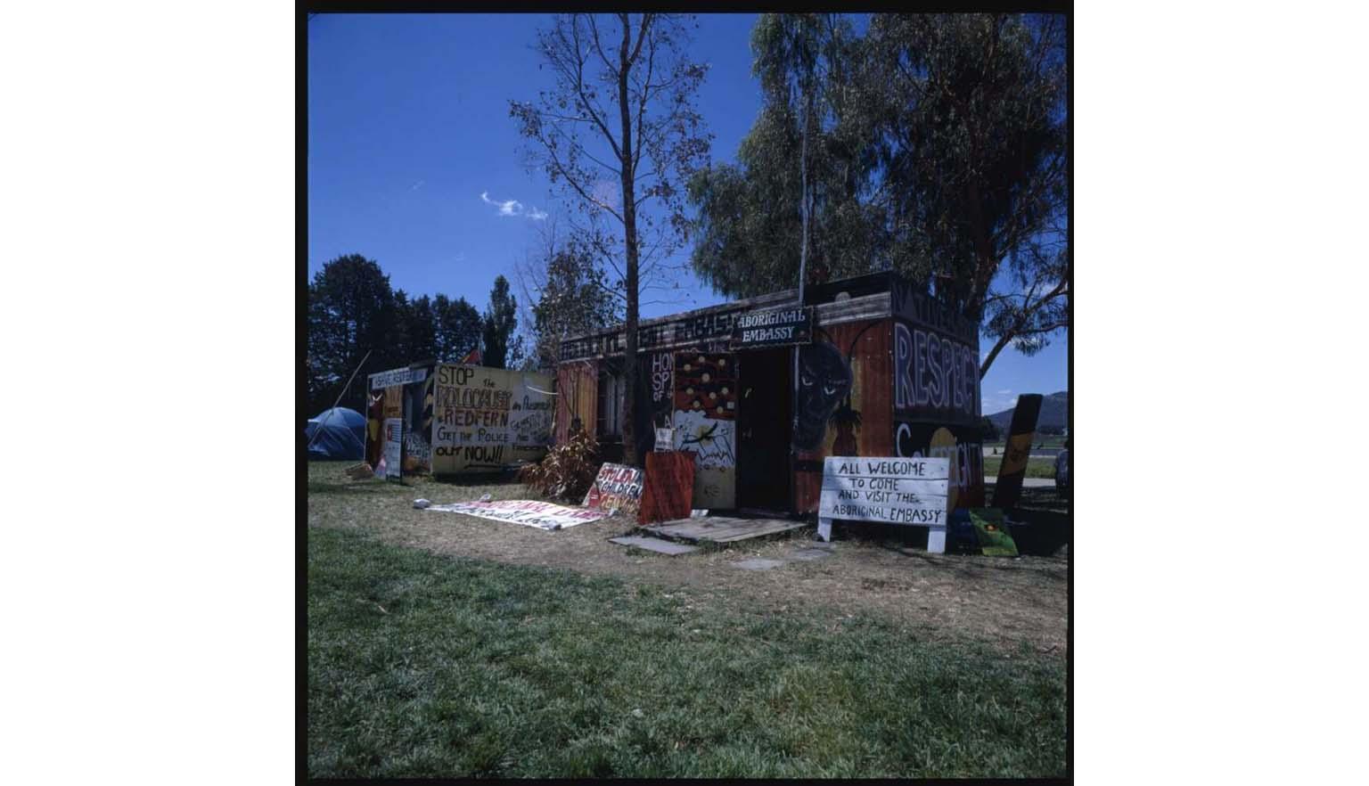 A photo of two tents decorated with painted words and Aboriginal art and a sign saying 'All welcome'.