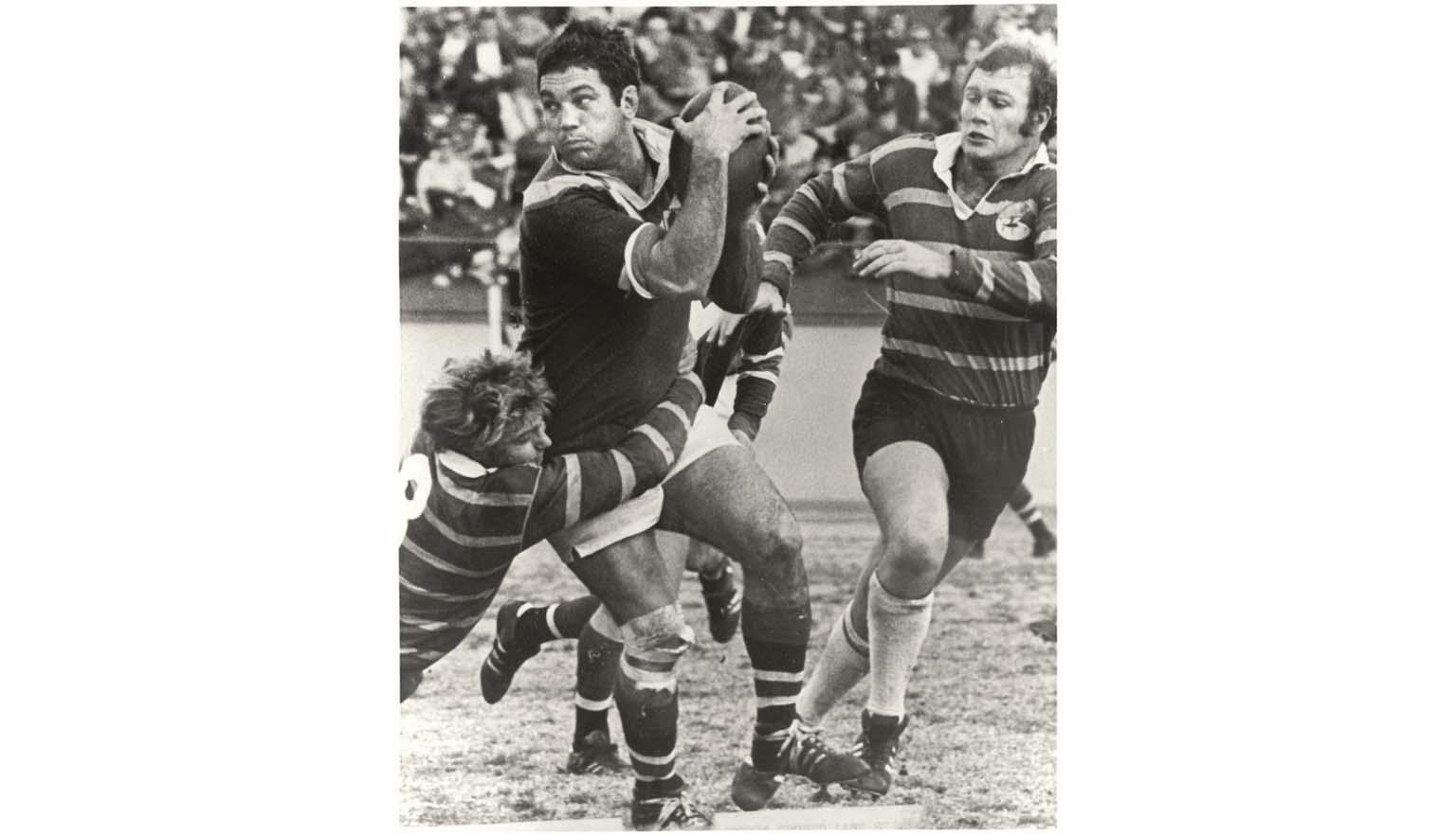 Black and white photo of Rugby League player, Arthur Beetson, looks for a team mate before passing the ball