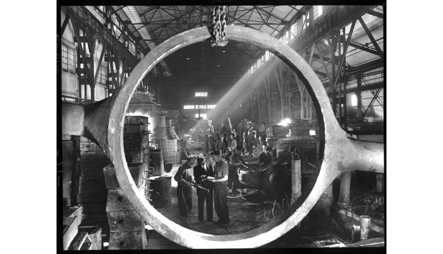 Photograph of employees at BHP steelworks, Newcastle. The dressing end of the steel foundry, viewed through a cast steel tilting frame of a slag pot.