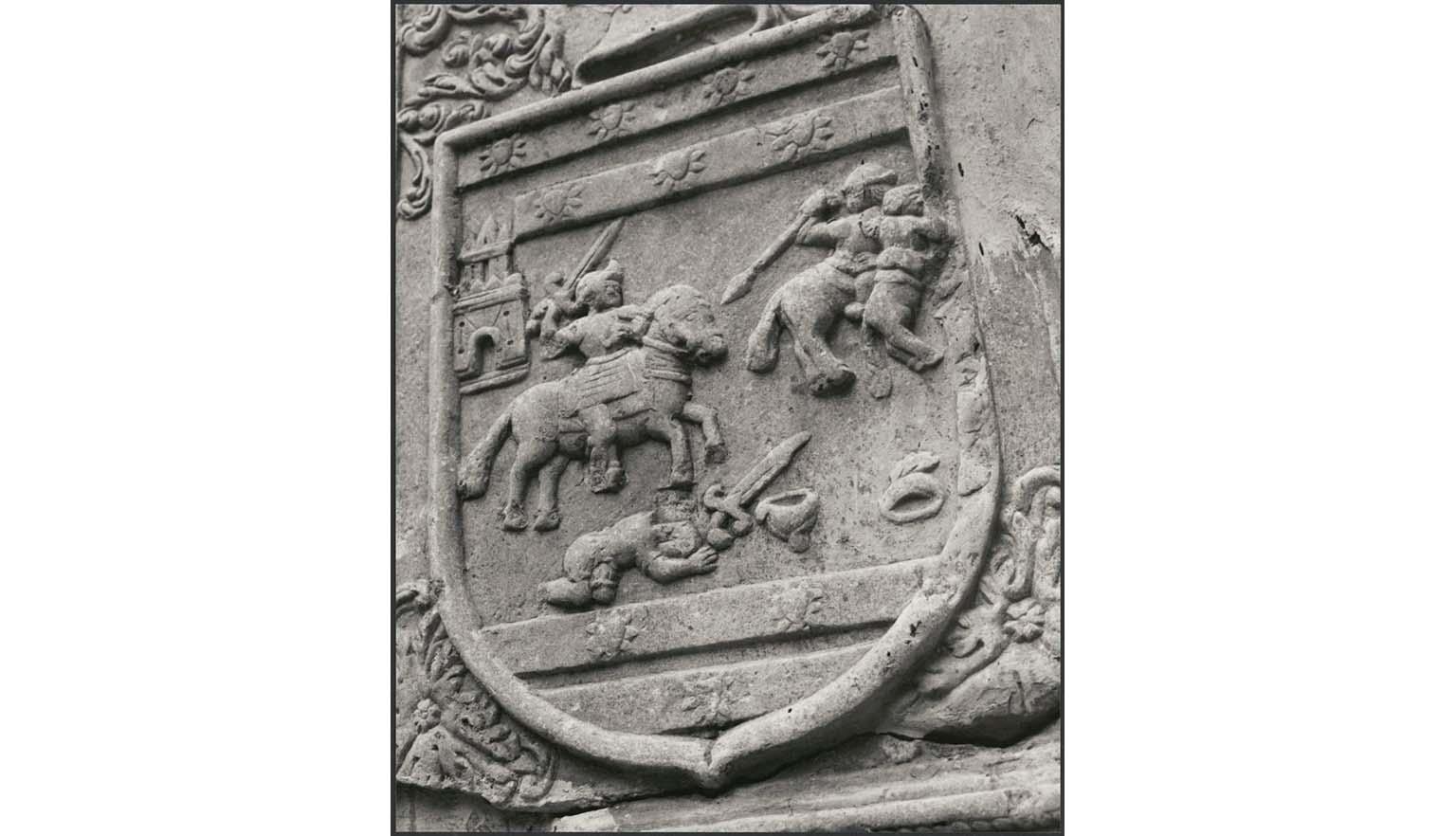 A close up photo of an architectural detail on a building. The detail is a knight on horseback fighting. The image is enclosed in a shield.