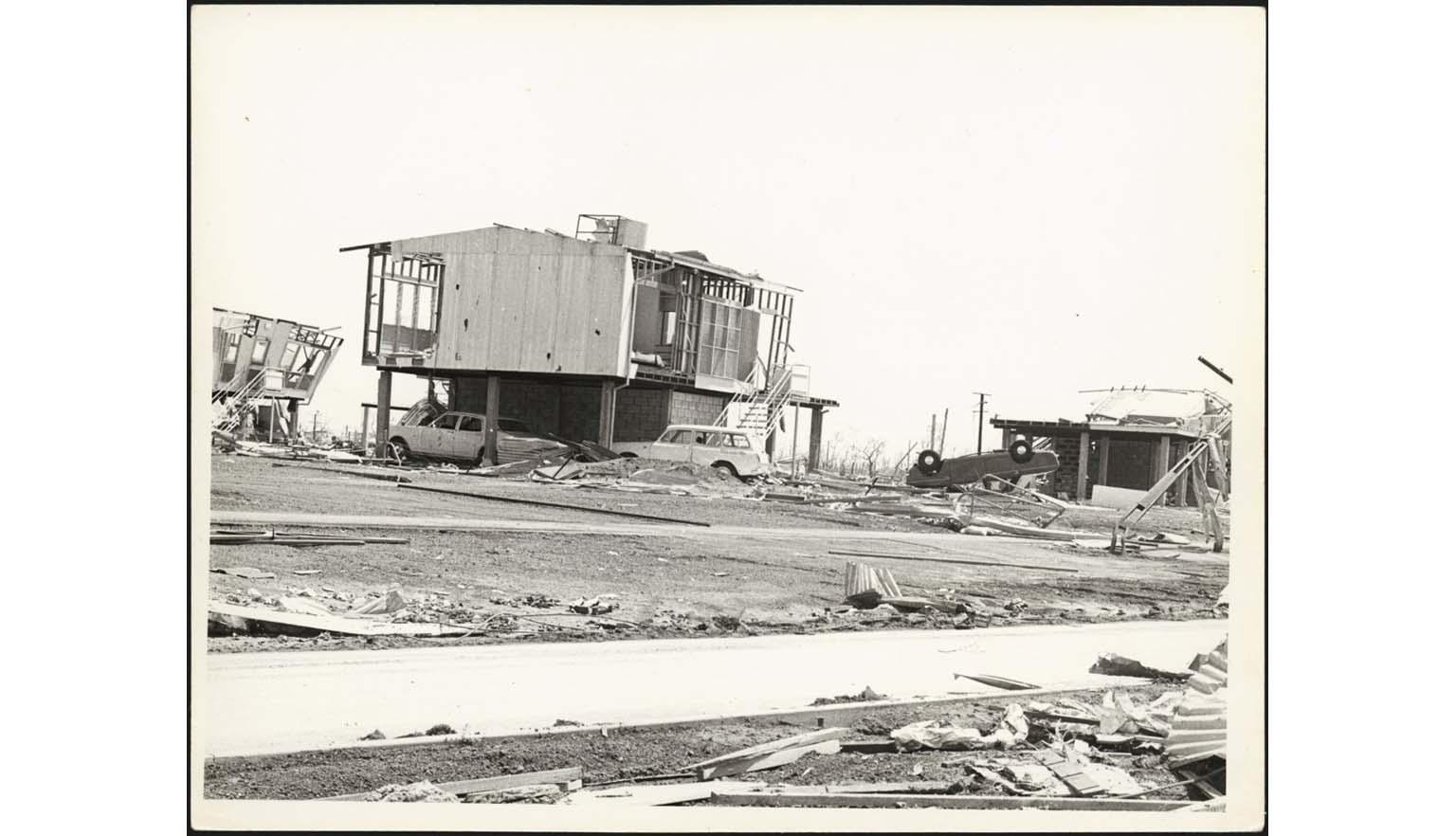 Black and white photo of houses and a car destroyed by a cyclone.