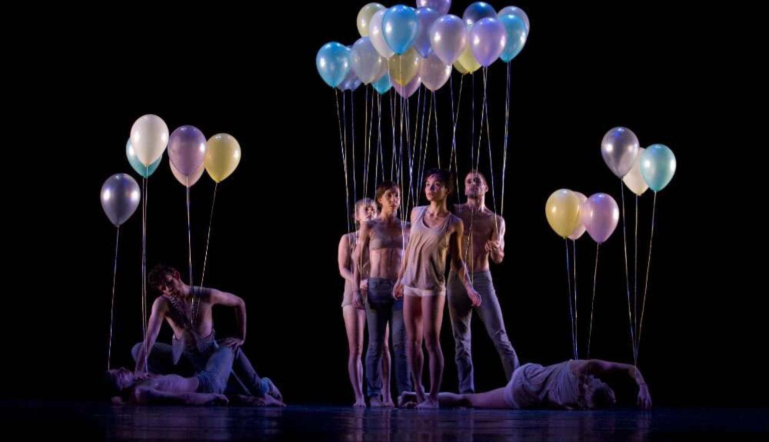 Dancers standing, crouching, and laying down holding balloons