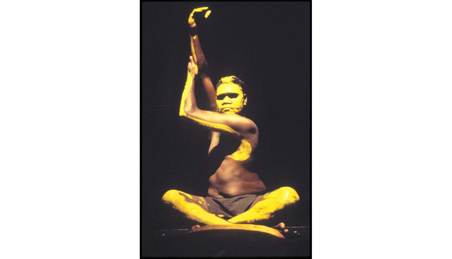 First Australians dancer sitting cross-legged with hands in the air