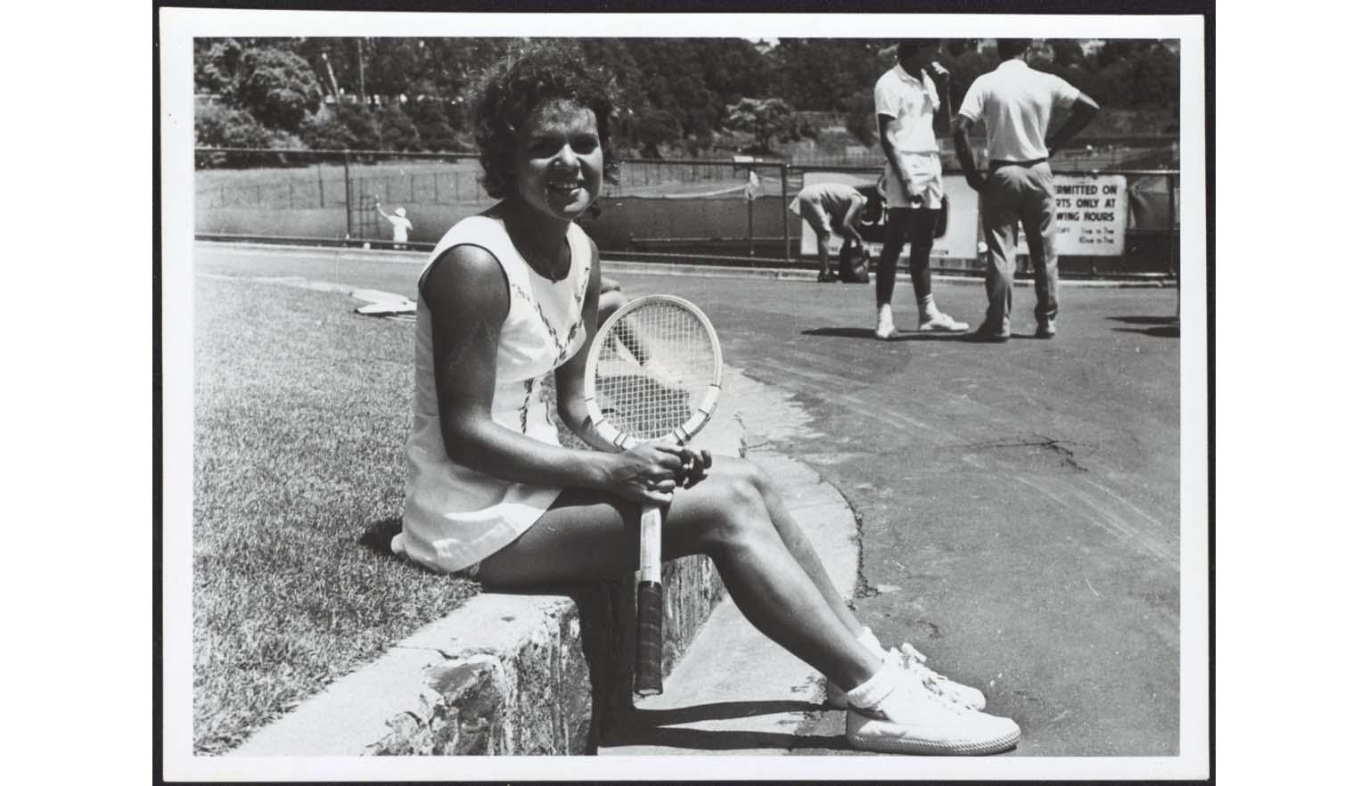 Black and white photo of Evonne Goolagong sitting holding a wooden tennis racket