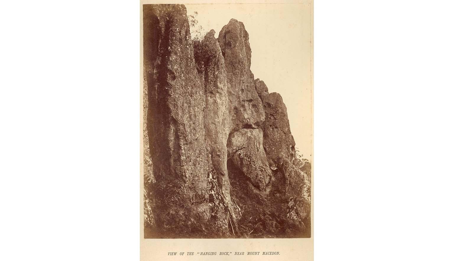 A sepia toned photo of a closeup of Hanging Rock, with words typed underneath saying ' View of the "Hanging Rock" near Mount  Macedon'