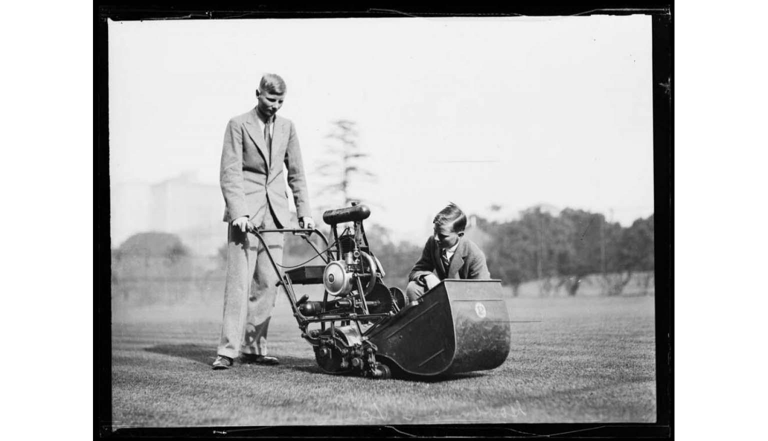 black and white photograph of two young men examining a lawn mower