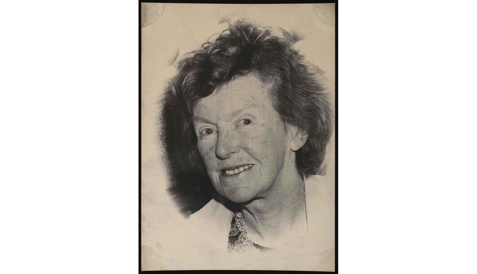 A black and white portrait photo of an elderly woman with a freckled face and red/dark coloured hair.