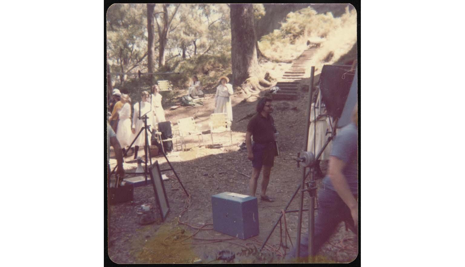 Filming equipment in bushland with group of girls in Georgian dress in background
