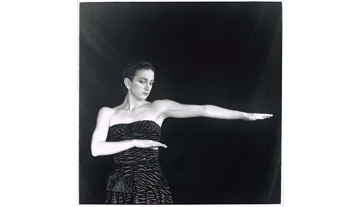 Ballerina Meryl Tankard strikes a pose. She is wearing a zebra print-esque dress. She is standing in front of a black curtain.