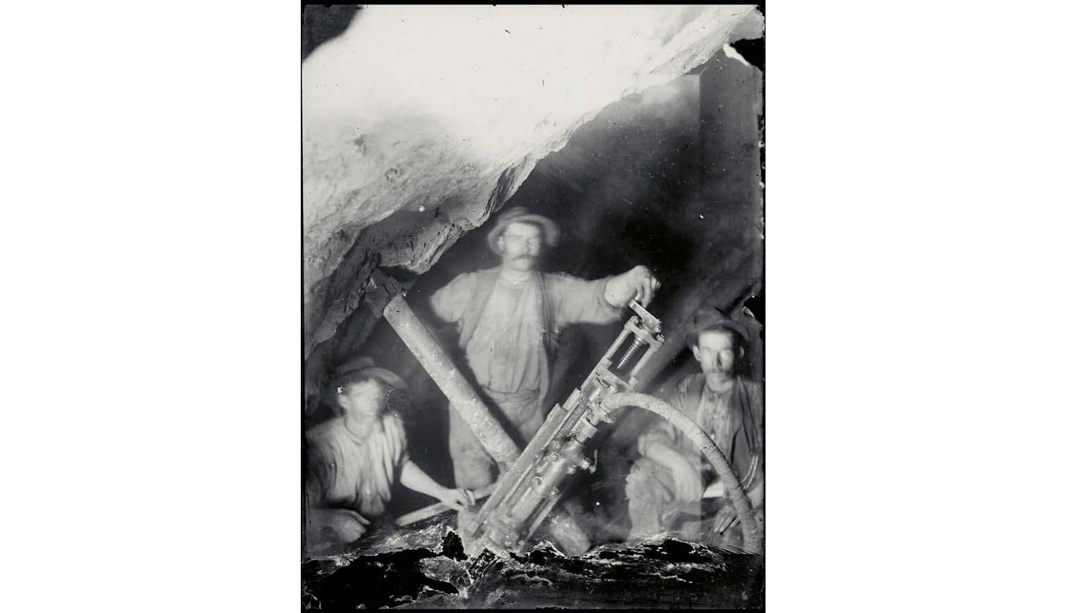 black and white photograph of three miners with an early pneumatic drill