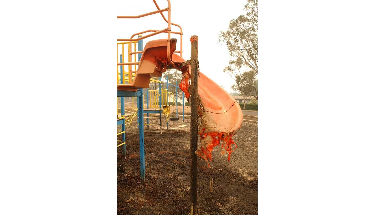 A children's playground slide is half melted after a fire burned through the playground. The surrounding metal of the playground is relatively untouched.