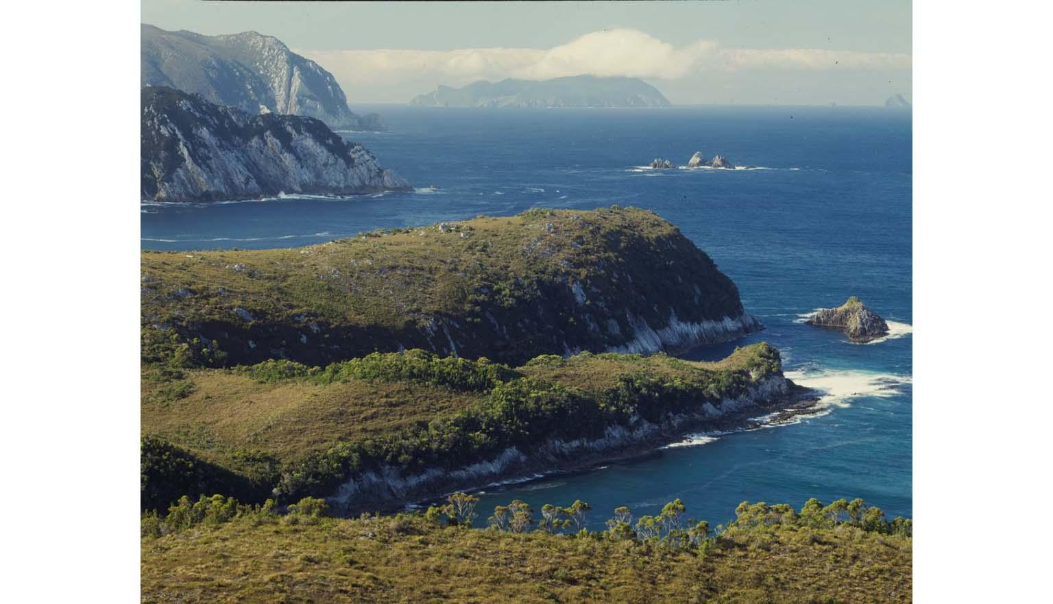 A scene of an ocean cliff. The ocean is dotted with craggy rocks. A series of cliffs stretch off into the distance.