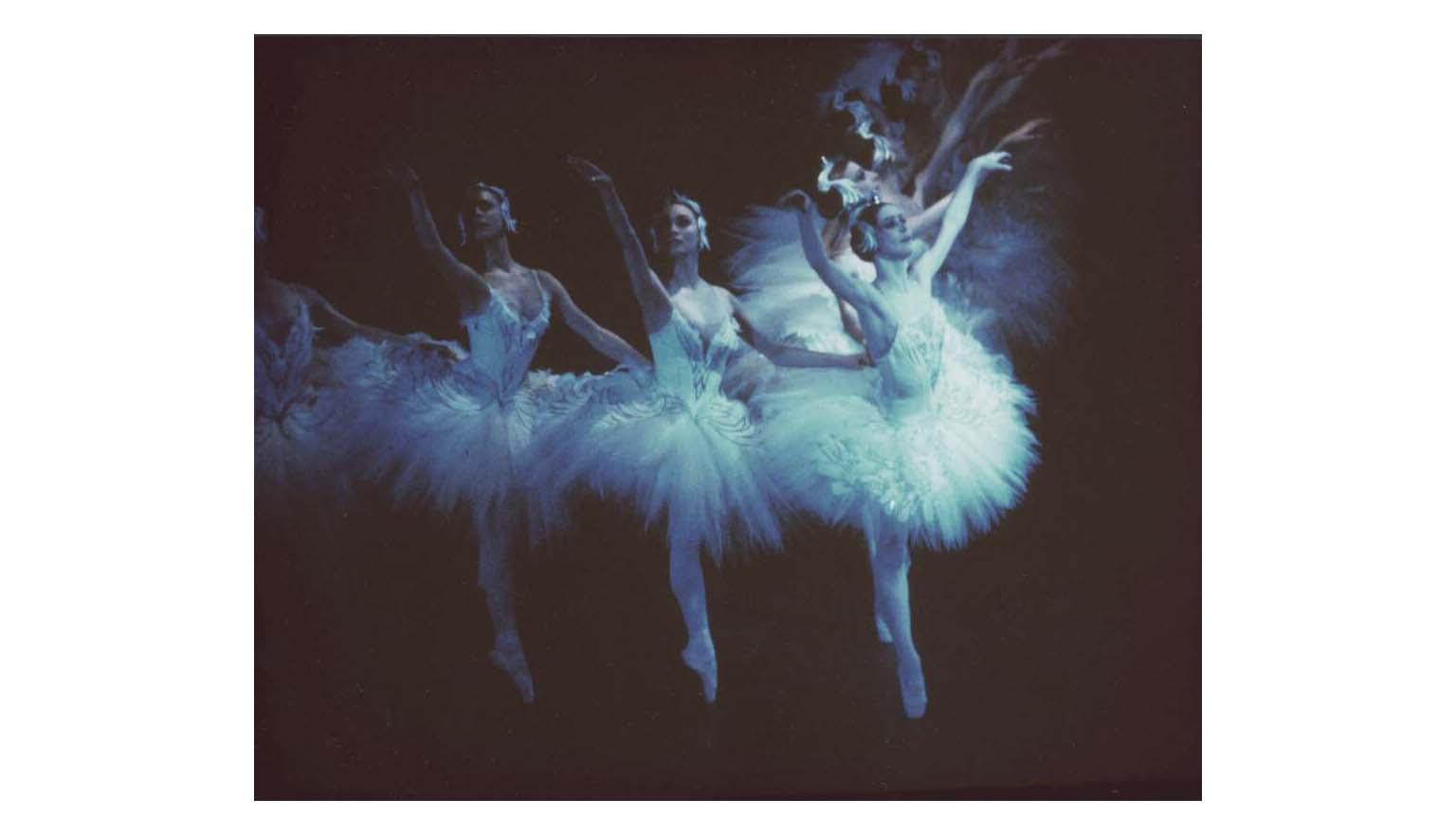Three ballerinas mid-movement in matching white tutus