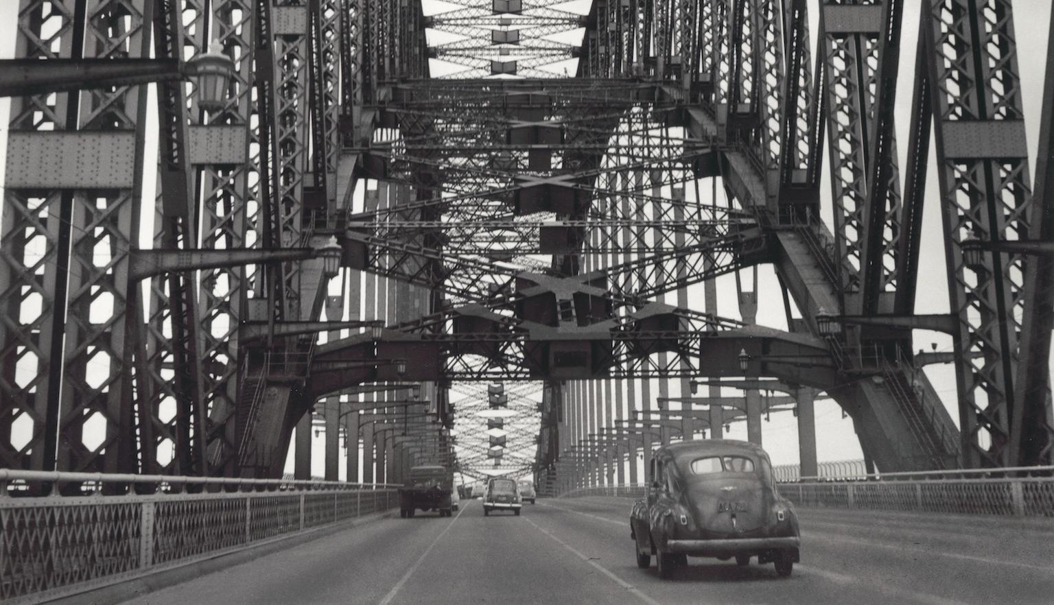 Black and white photo of cars crossing the Sydney Harbour Bridge taken from the middle of the road, 