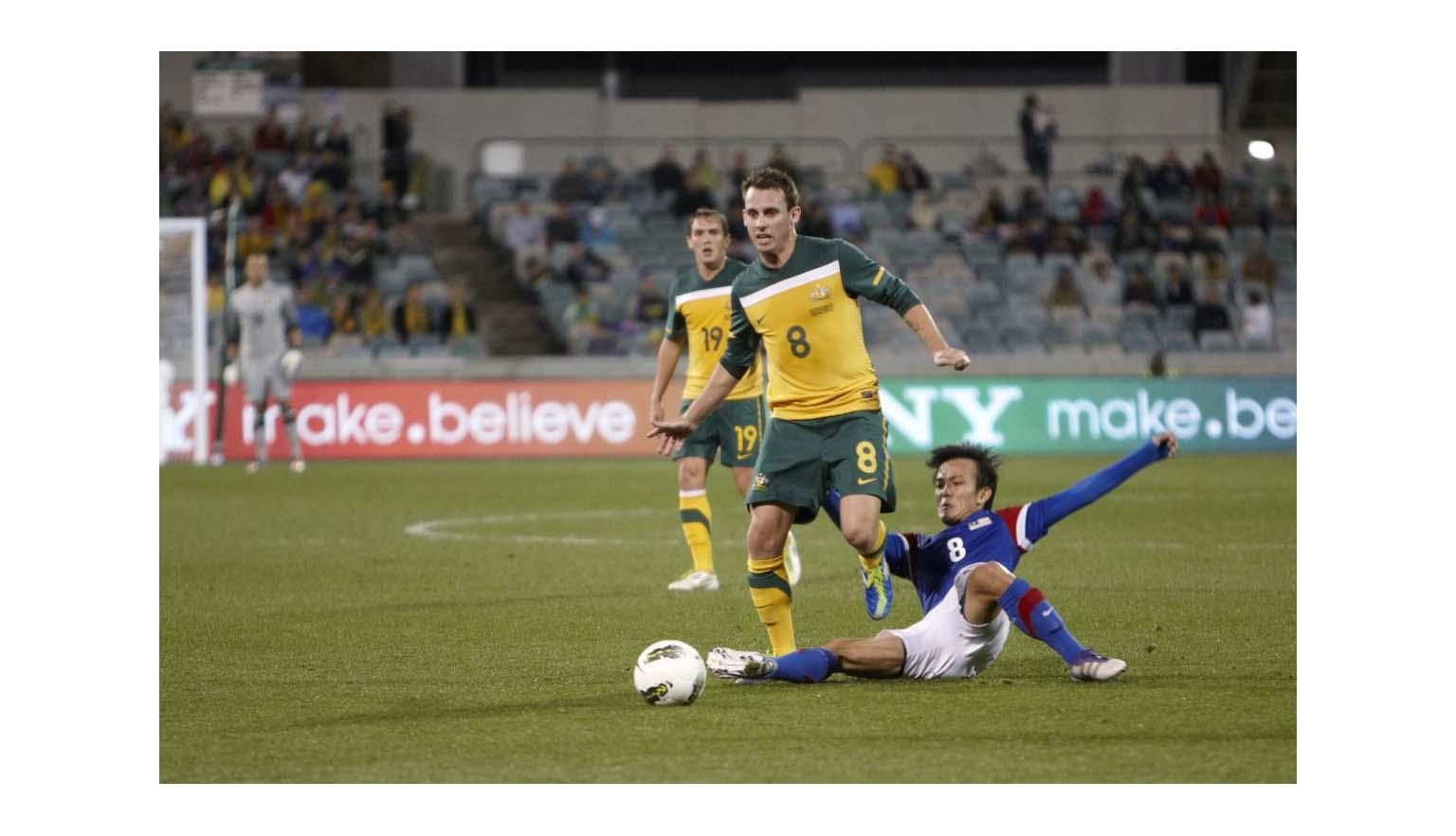 Photo of a Socceroos player being tackled by a Malaysian player