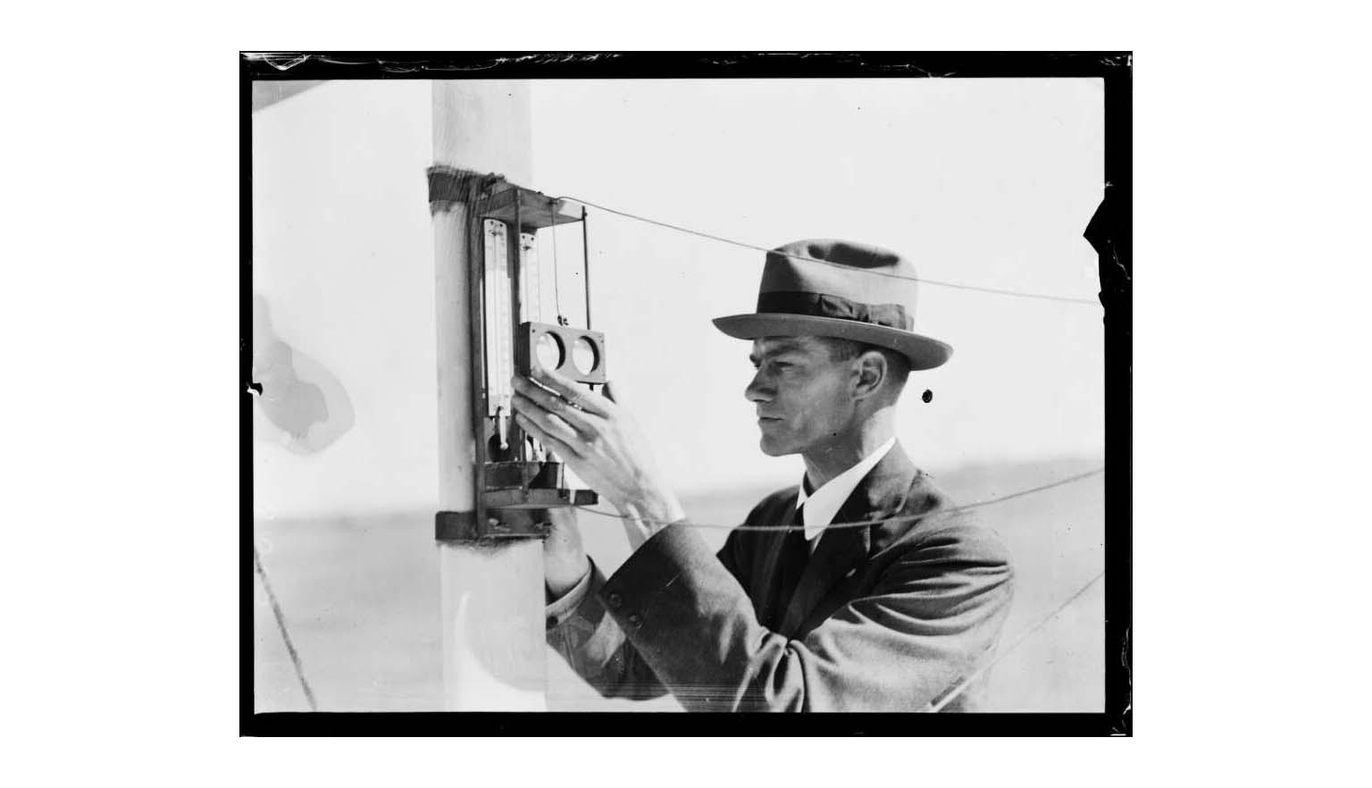 Black and white photo of a man in a hat reading thermometers