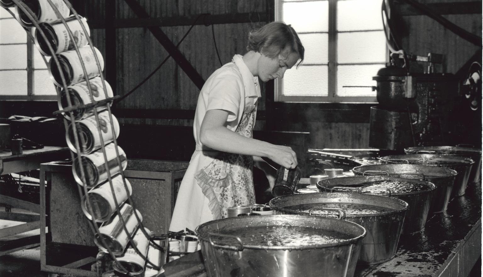 Woman pouring jam from large pots into tins n a factory
