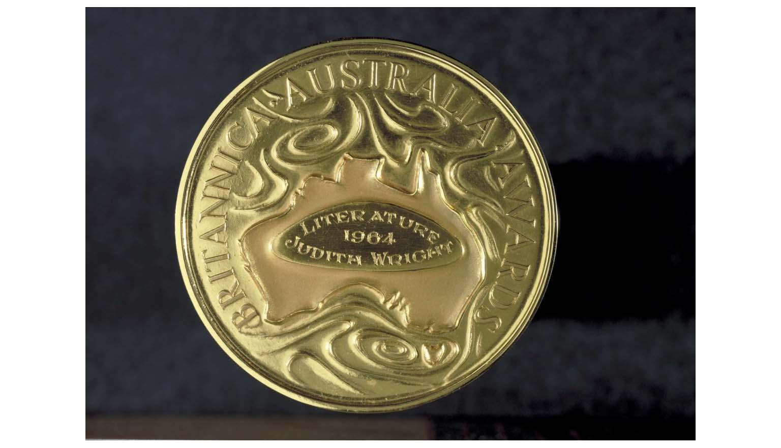 A photo of a gold medal showing a map of Australia surrounded by the words Britannica Australia Awards. In the middle of the map of Australia are the engraved words 'Literature, 1964, Judith Wright'.