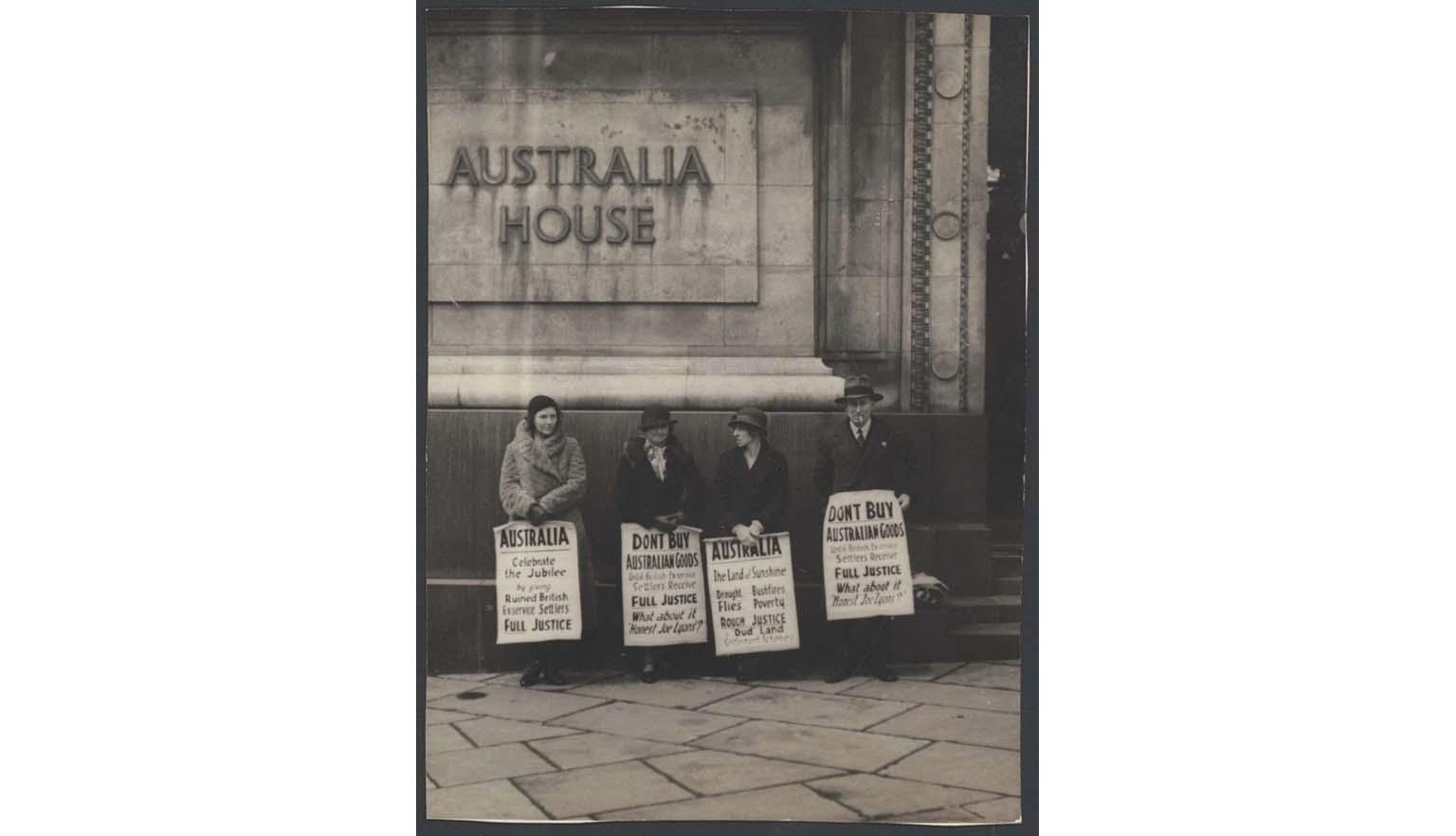 Black and white photo of three women and one man in winter clothes standing outside a building with signs protesting the treatment of British soldier settlers in the Australian War Service Land Settlement Scheme