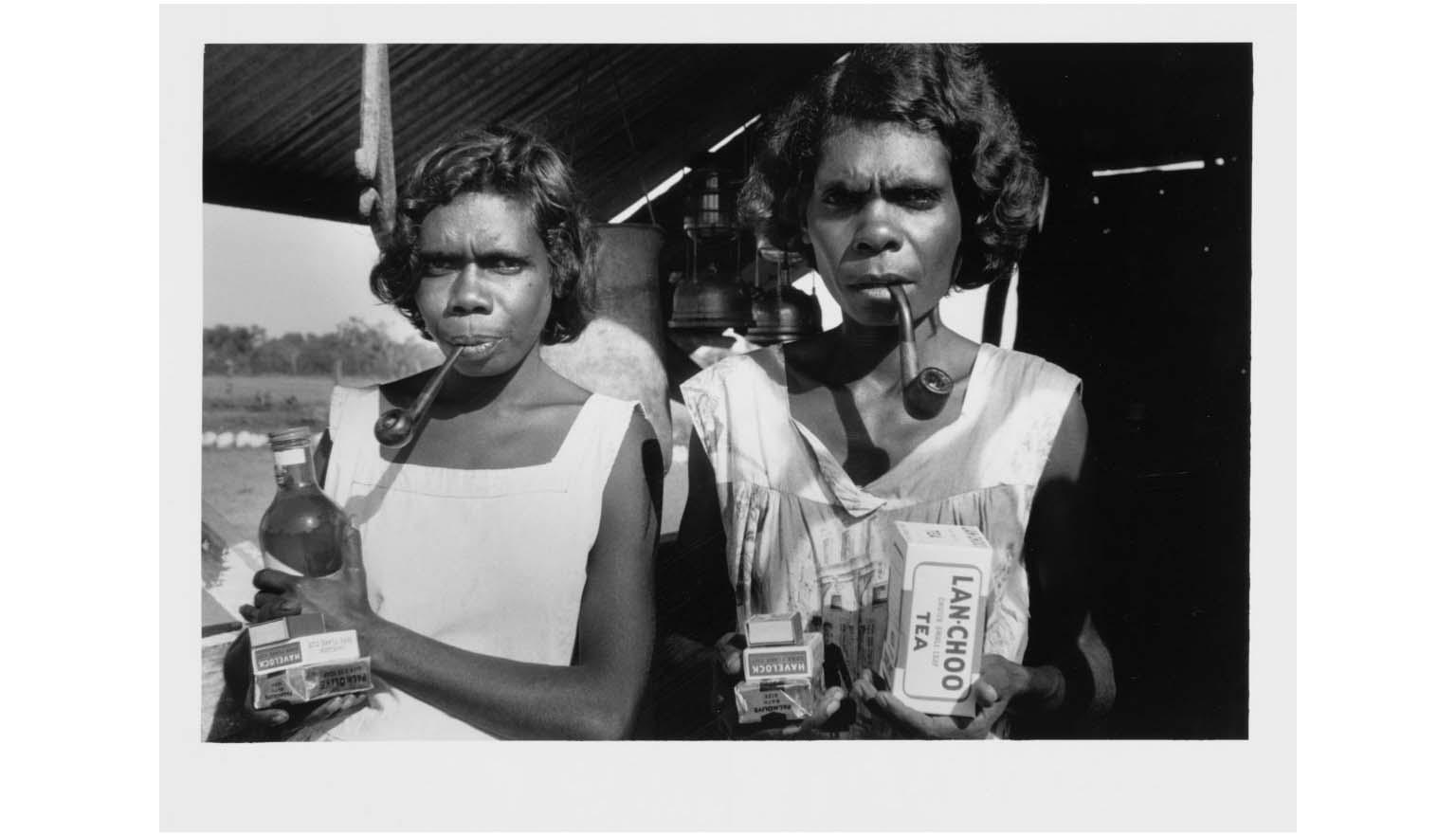 black and white photograph of two young Aboriginal women with pipes and groceries