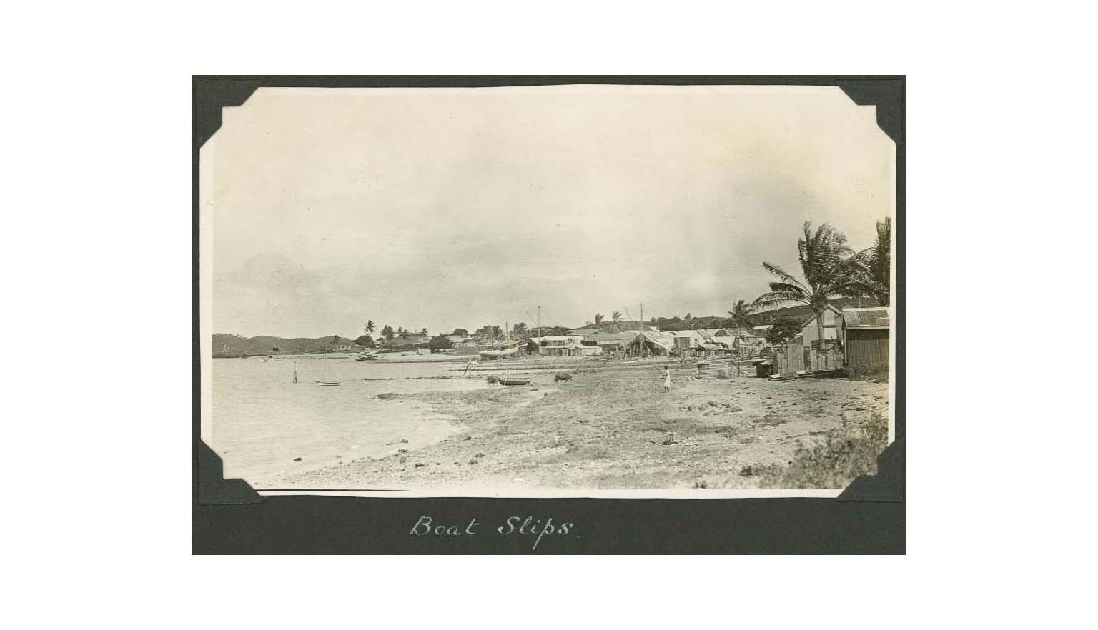 sepia photo of a settlement next to water with some boats pulled up onto land
