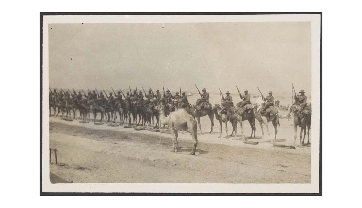 Sepia photograph of World War One soldiers mounted on camels lined up for inspection on the sand