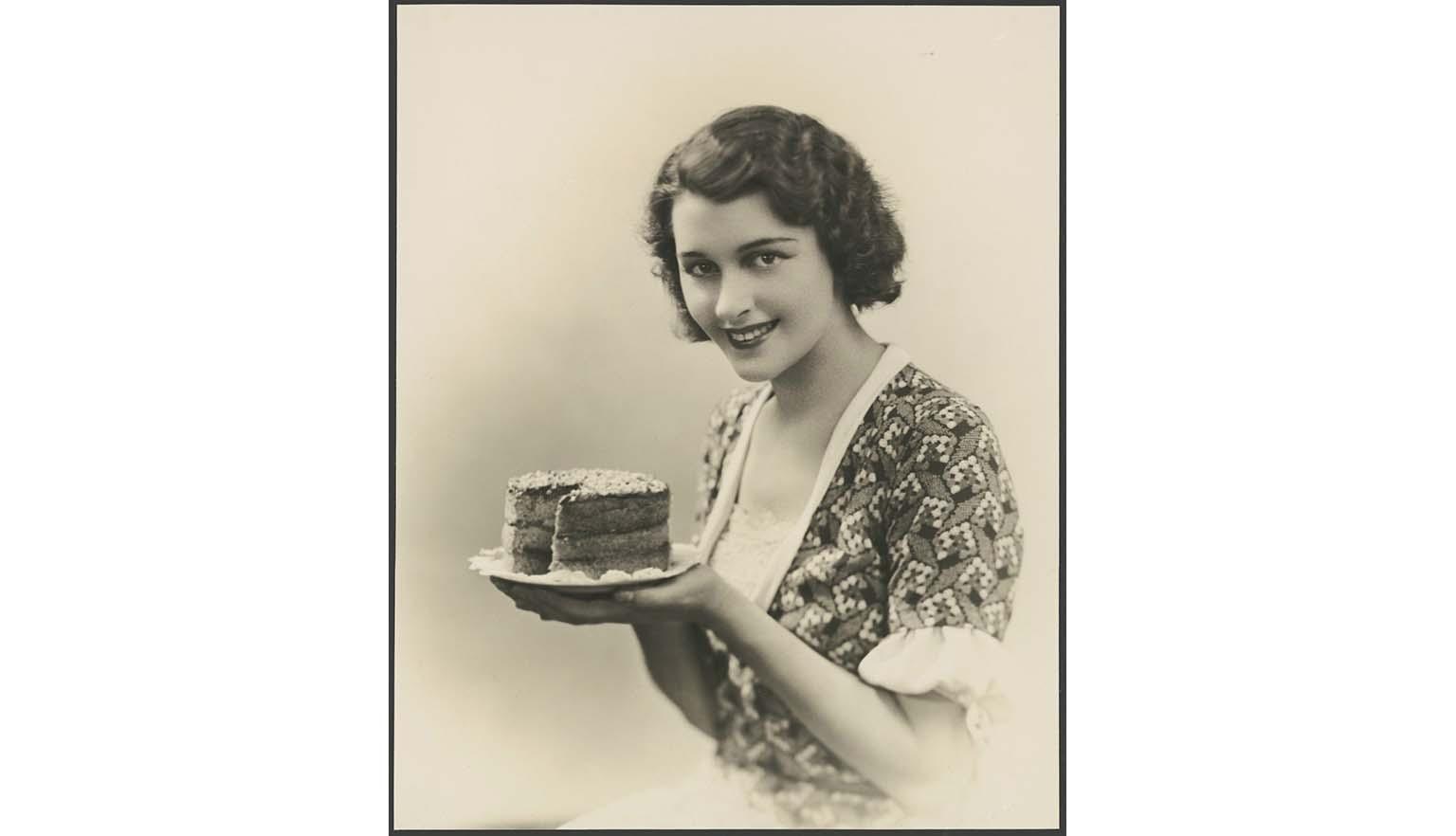 black and white photograph of a woman holding up a small cake with a slice taken out