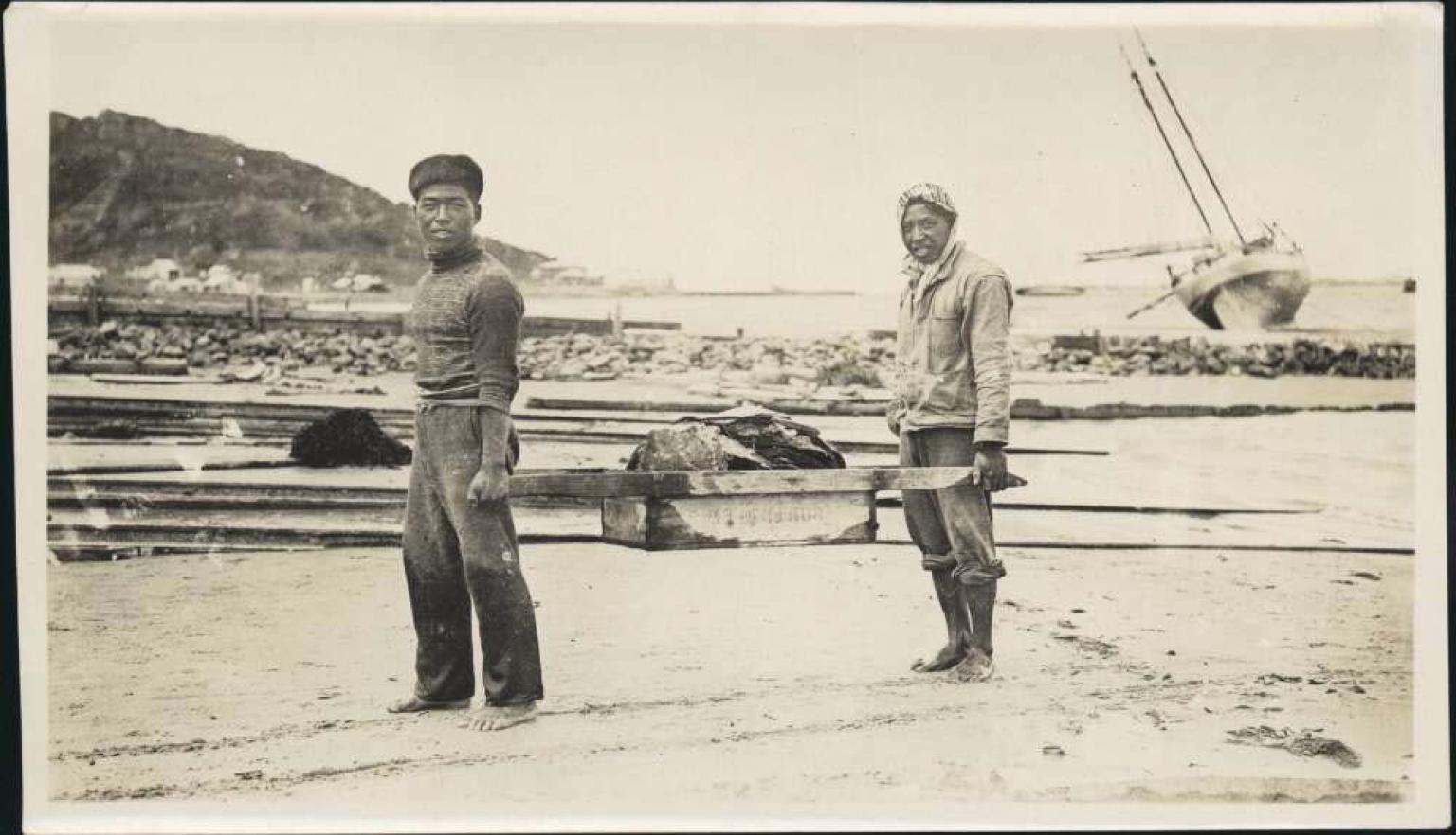 sepia photo of two men carrying a load of shells