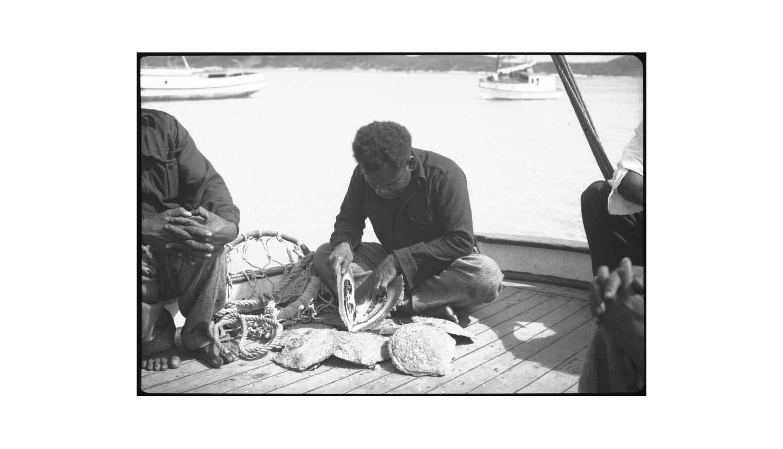 black and white photo of a man sitting on a boat deck opening shells