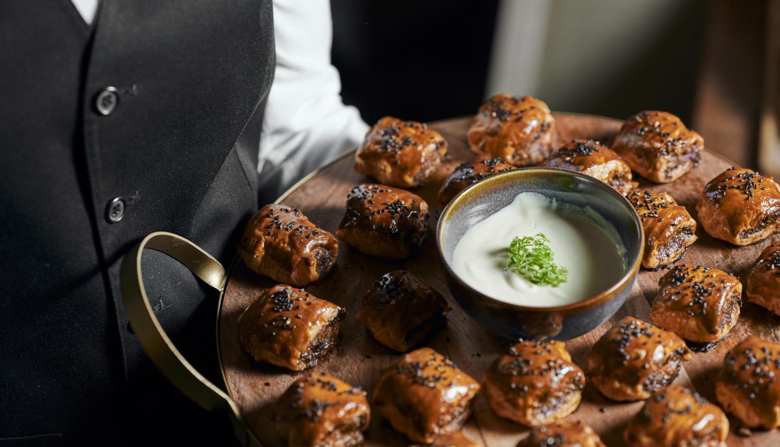 Server with a tray of cooked sausage rolls