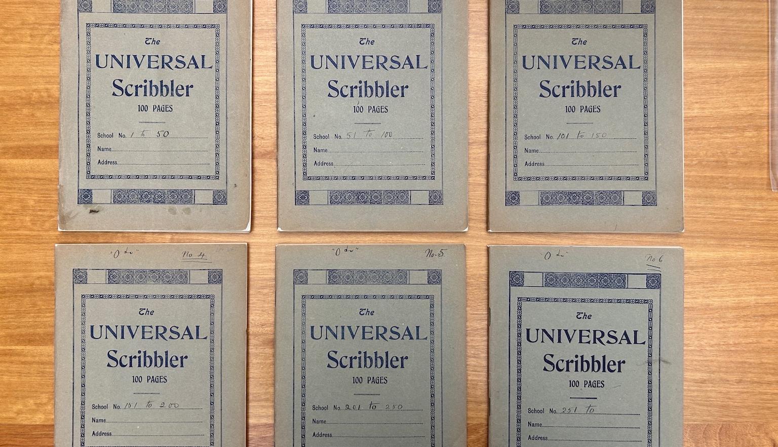 Six matching notebooks lined up, with three on the top row and three on the bottom, sitting on a wooden desk