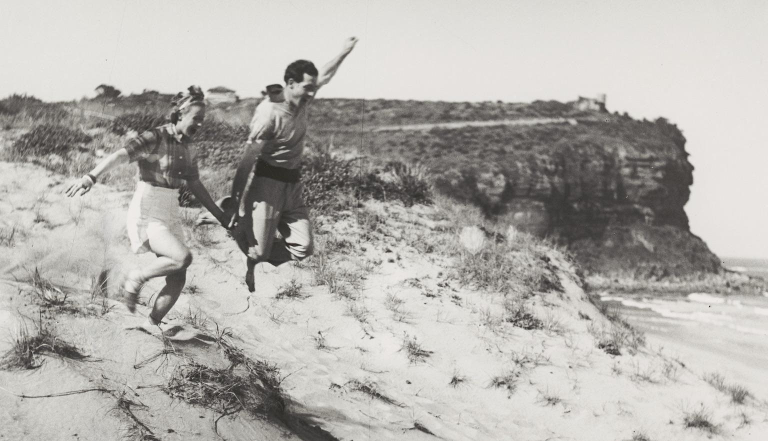 Man and woman holding hands and running down dunes at the beach