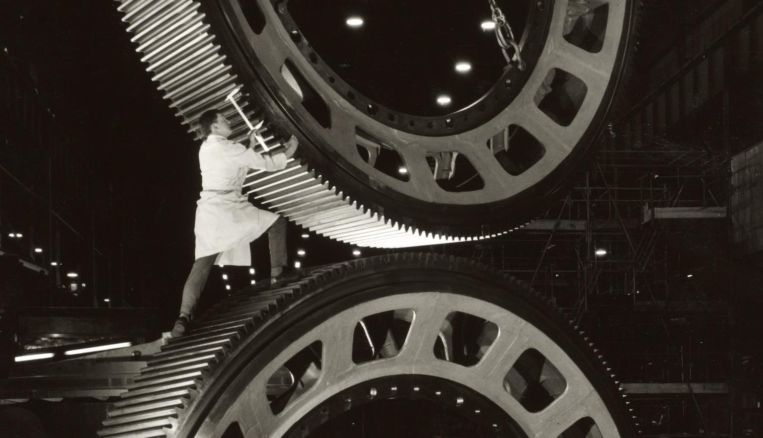 Man standing on top of a large semi-circle shaped piece of metal, guiding another being placed on top